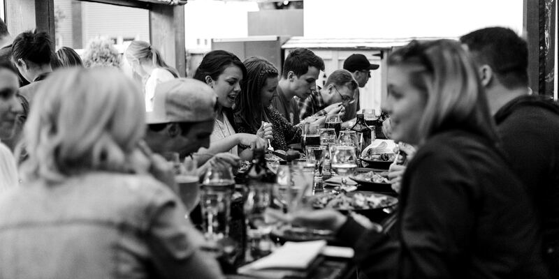 Neighbors laughing and talking together around a long table at a busy local restaurant