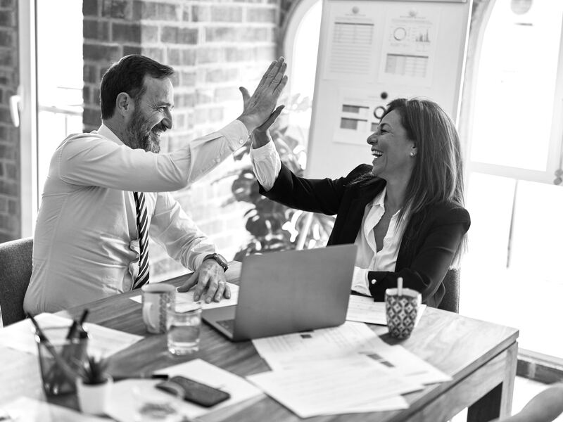 Two colleagues sharing a high five across a desk after a successful meeting