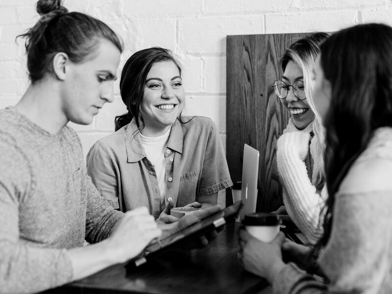 Four friends smiling and talking together over coffee at a cafe table